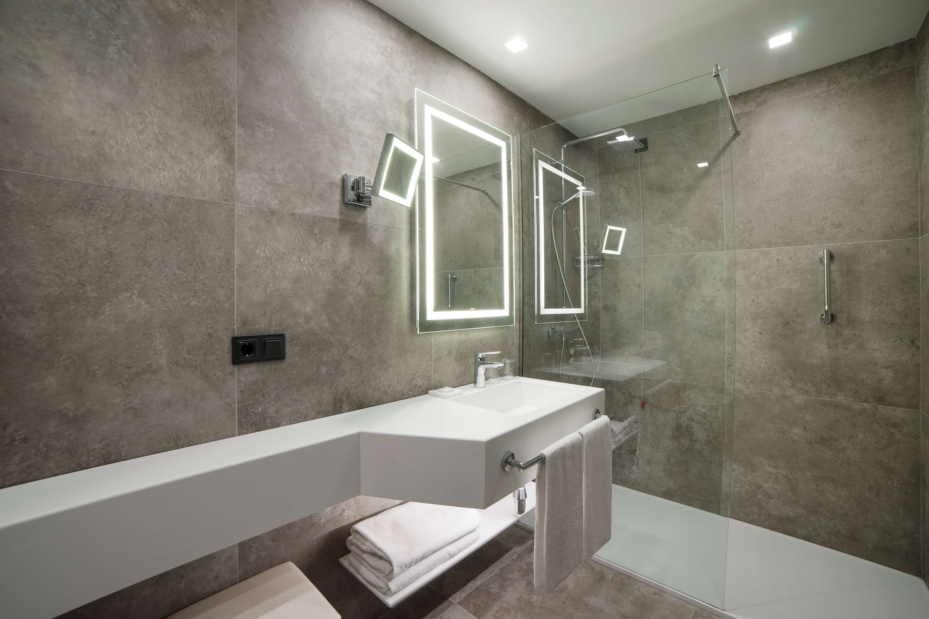 Une salle de bain moderne avec un grand miroir, un lavabo blanc et une douche à parois de verre.