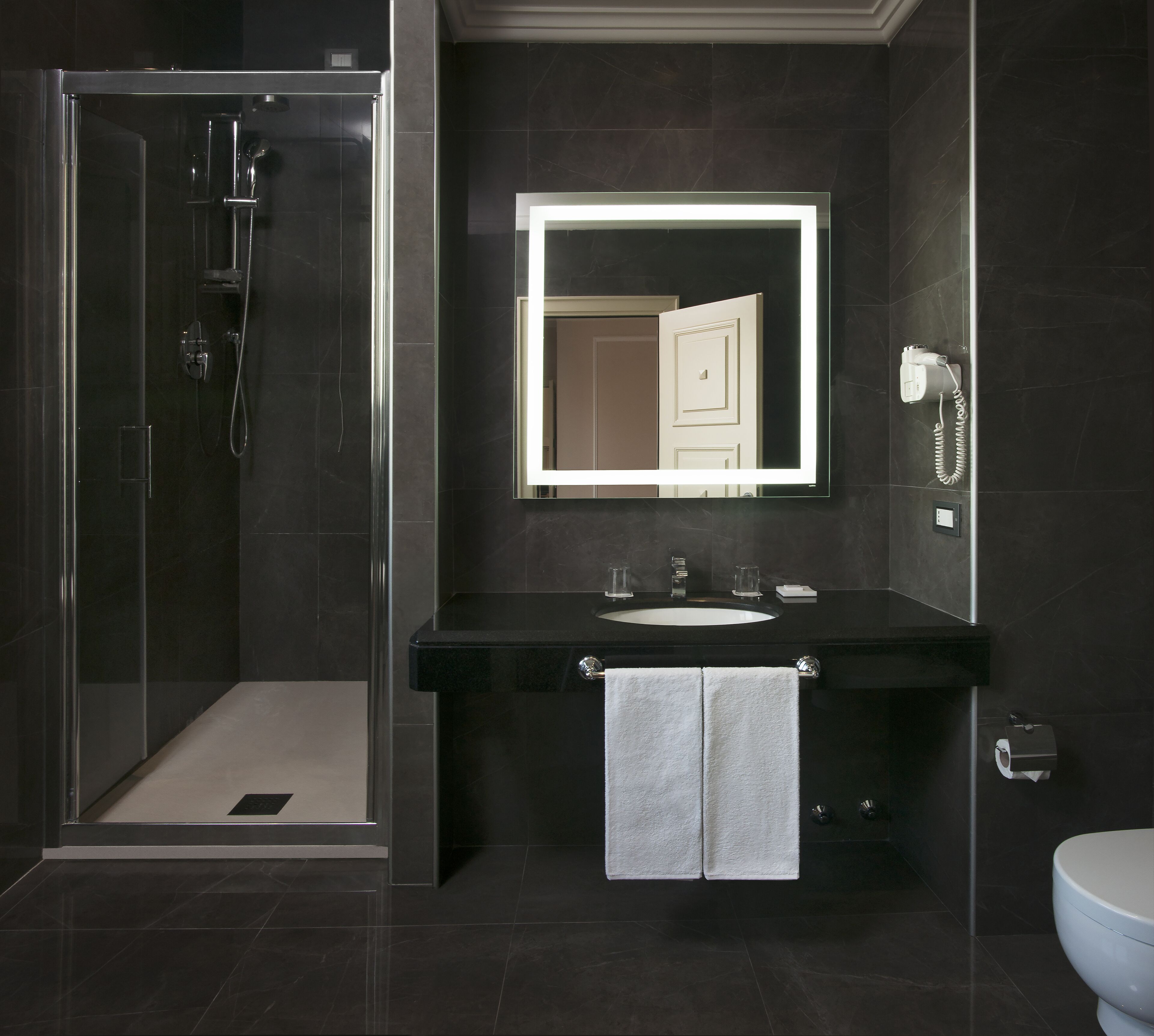 Un baño moderno con ducha envuelta en cristal, un lavabo negro y un espejo sobre él.