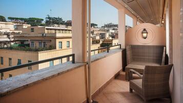 A balcony with a wicker chair, a view of surrounding buildings, and a wall-mounted light fixture.