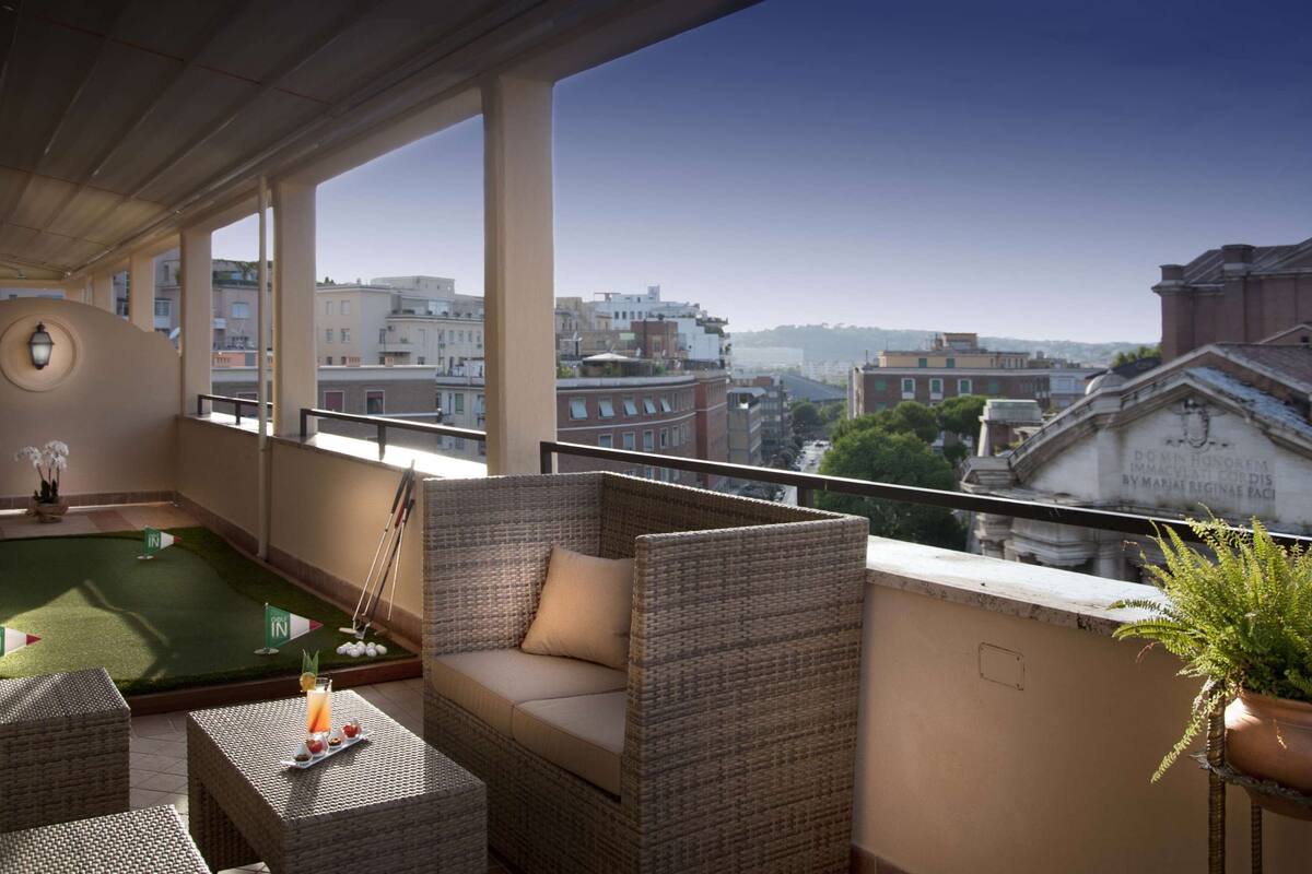 A balcony with a pool table, wicker furniture, and a view of city buildings.