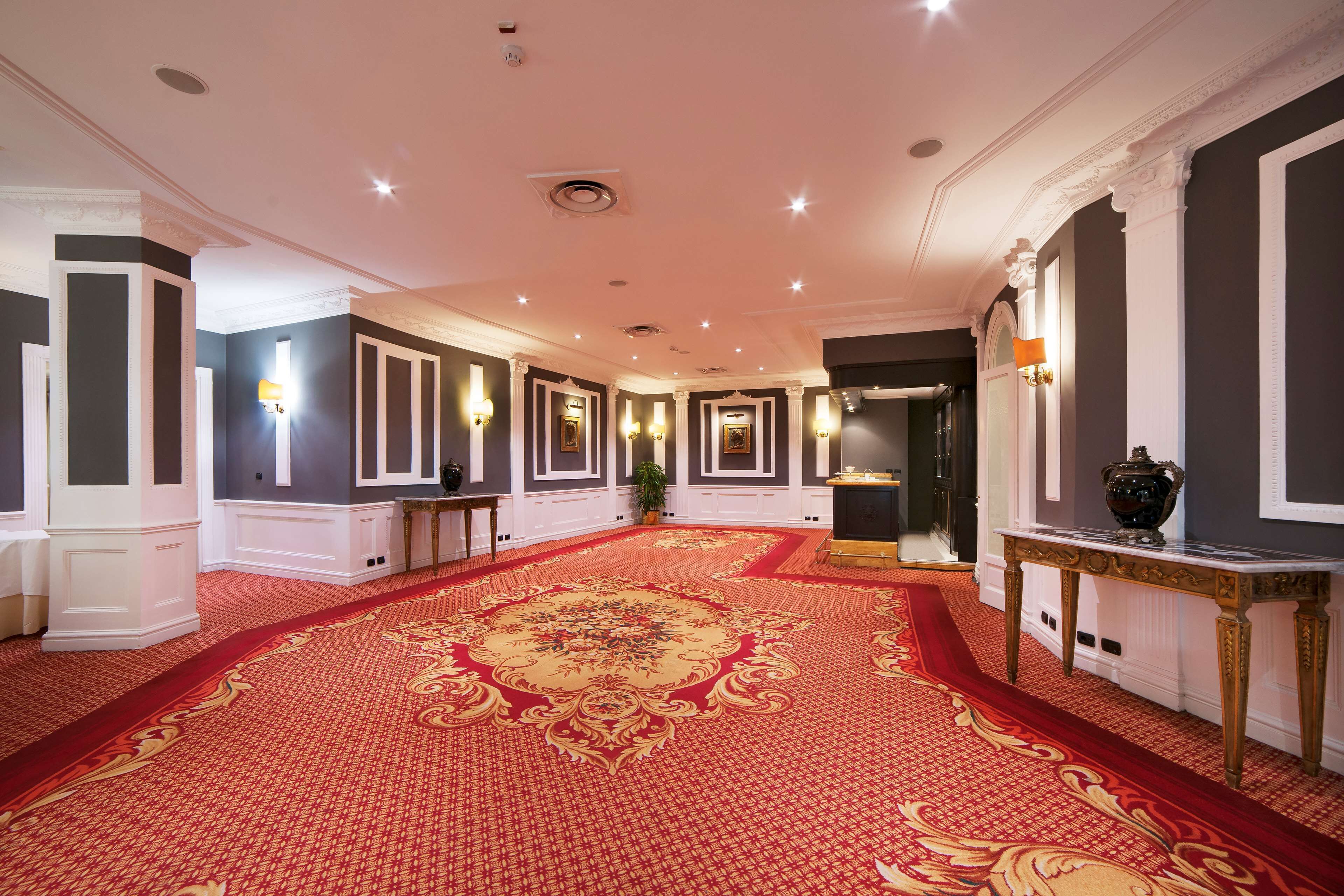 A grand hallway with a red carpet, white columns, and wall sconces.