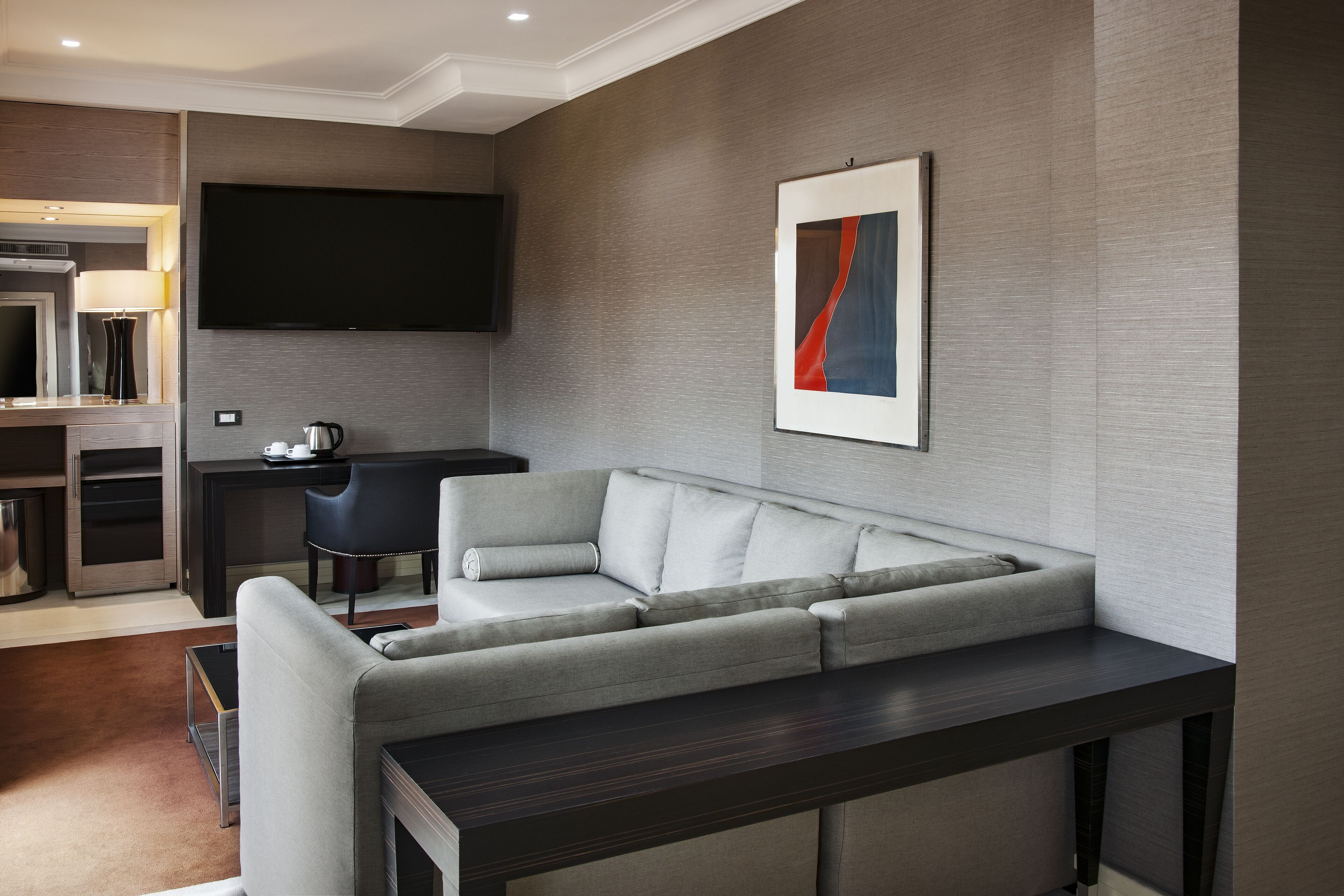 Ein modernes Wohnzimmer mit einem grauen Ecksofa, einem flachbildfernseher an der Wand und einem zeitgenössischen Kunstwerk.