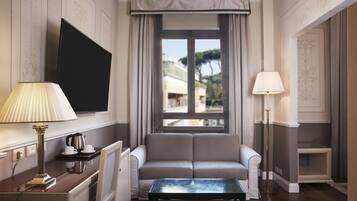A hotel room with a sofa, a coffee table, a TV mounted on the wall, and a window with curtains.