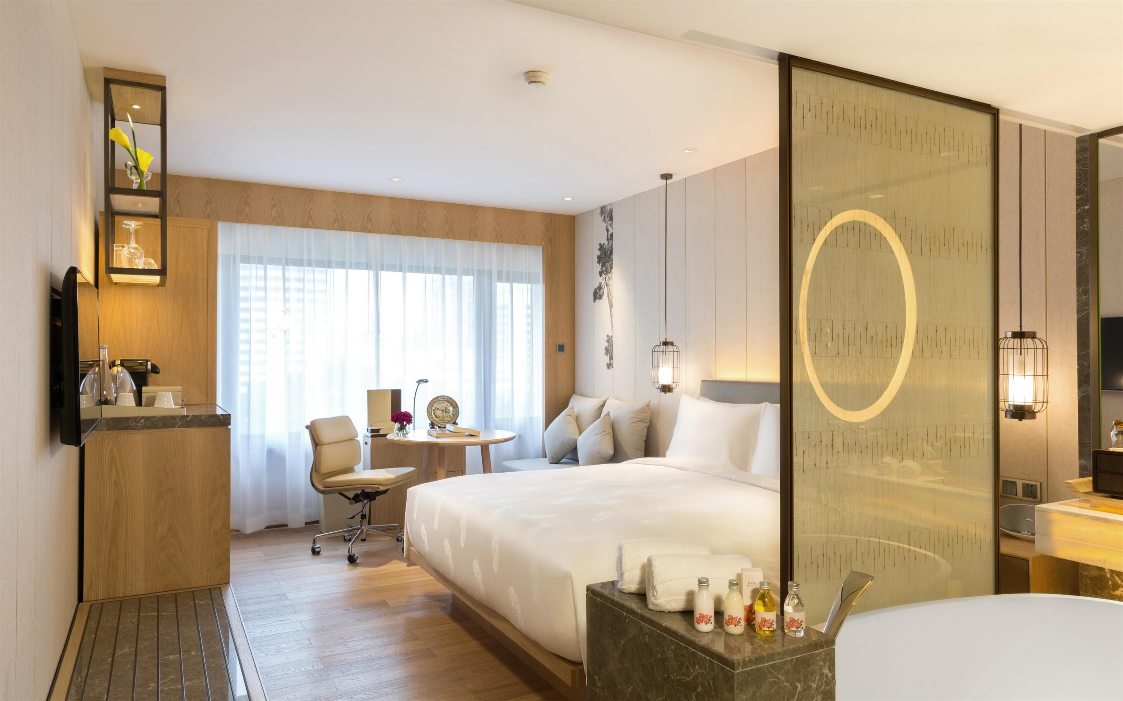 A hotel room with a bed, a desk, a chair, a small table, and a mirror.