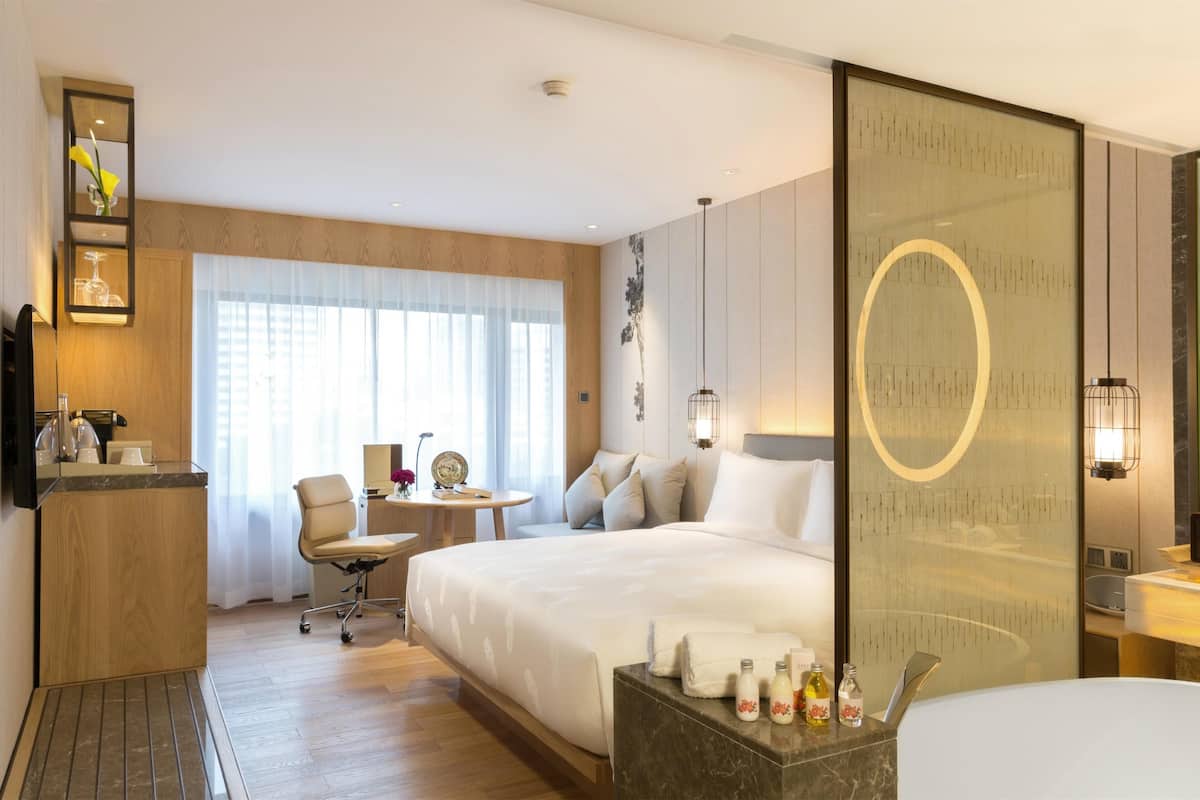 Een hotelkamer met een bed, een bureau, een stoel, een klein tafeltje en een spiegel.