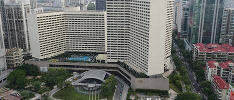 A large, modern hotel with a distinctive curved facade, surrounded by a well-maintained courtyard and a busy urban street.