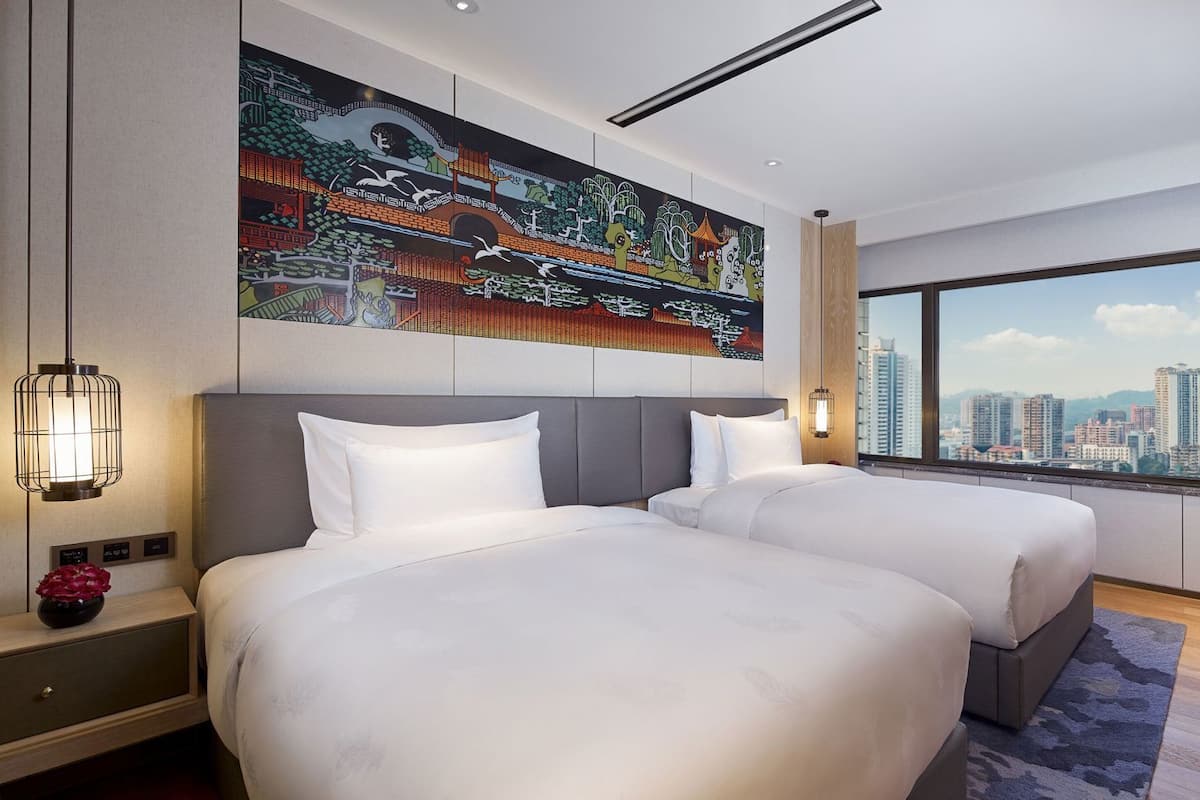 Ein modernes Hotelzimmer mit zwei Betten, Blick auf die Stadt, einem großen Wandgemälde und einem Fernseher an der Wand.