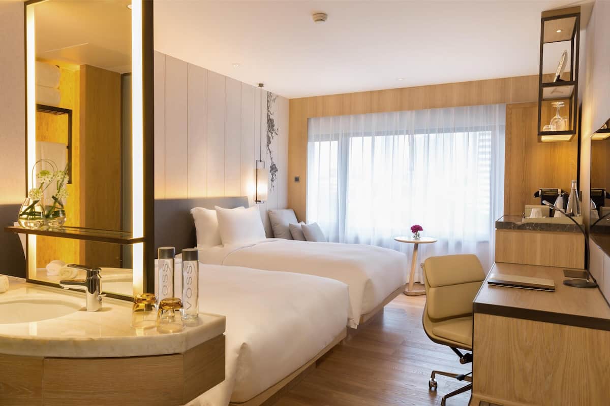 Hotelkamer met een groot bed, een bureau, een stoel, een badkamer met een wastafel en spiegel, en een groot raam met gordijnen.
