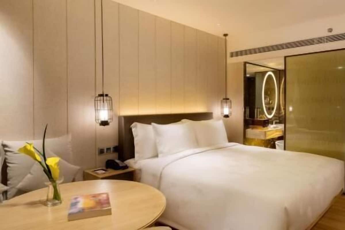 Een hotelkamer met een bed, nachtkastje, lamp en een spiegel.