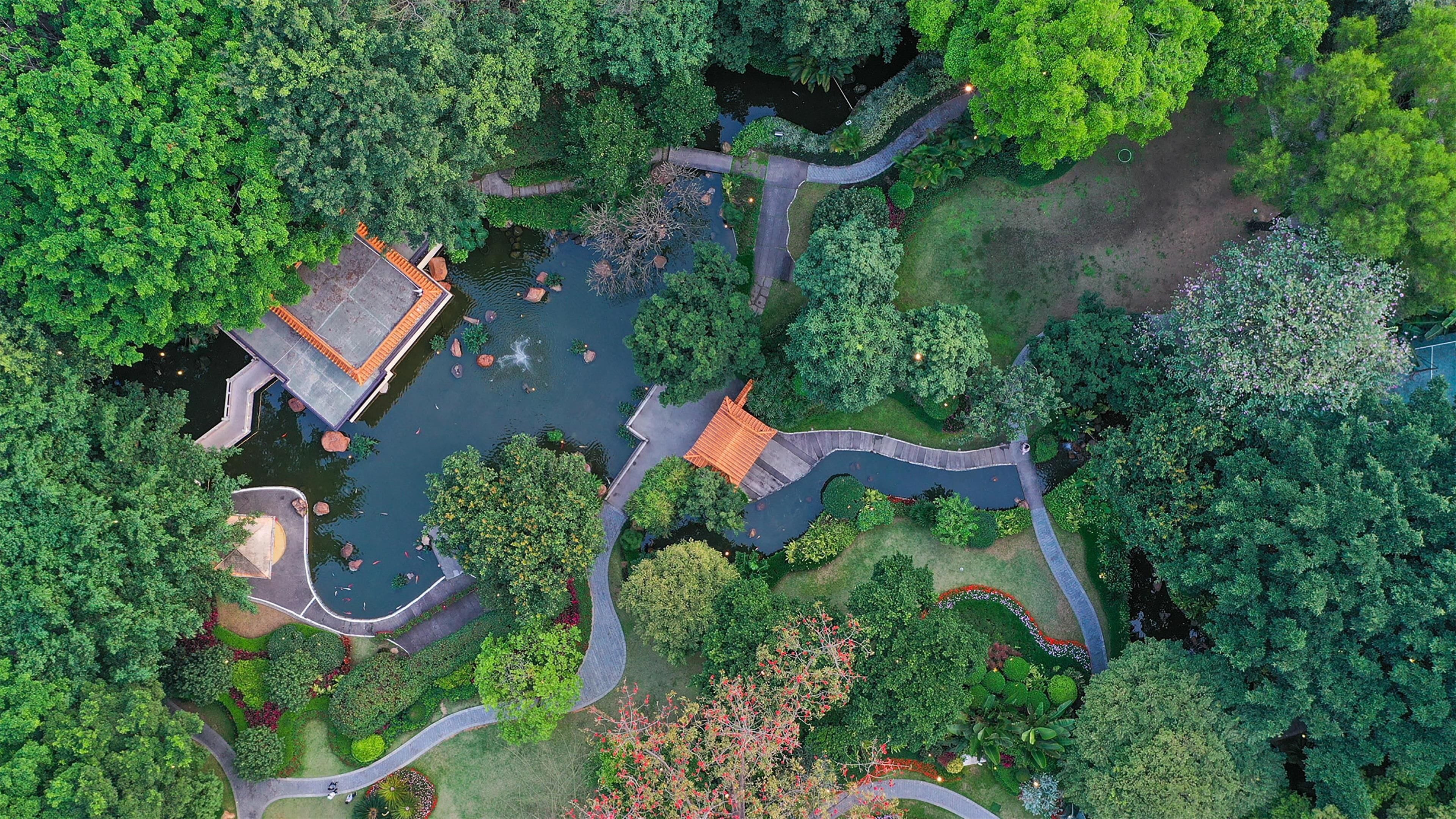 An aerial view of a park with pathways, a pond, and a traditional building with a tiled roof.