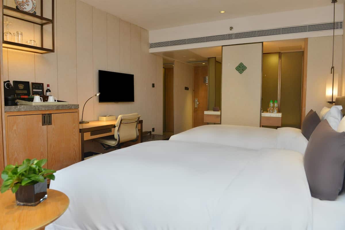 Een hotelkamer met een bed, bureau, stoel, televisie en een kleine plant.