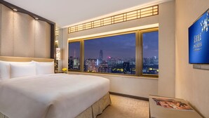 Een hotelkamer met een groot bed, uitzicht op de stad 's nachts en een televisie aan de muur.