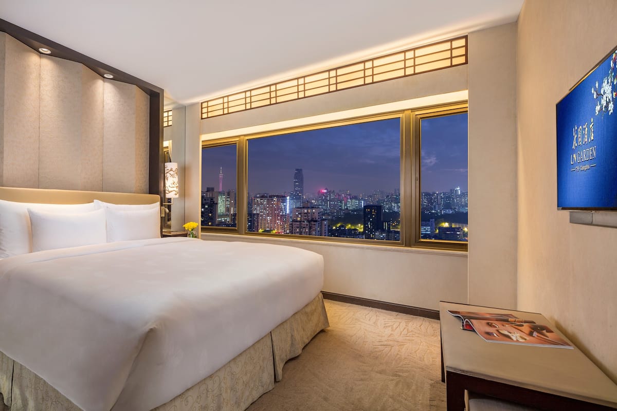 Een hotelkamer met een groot bed, uitzicht op de stad 's nachts en een televisie aan de muur.
