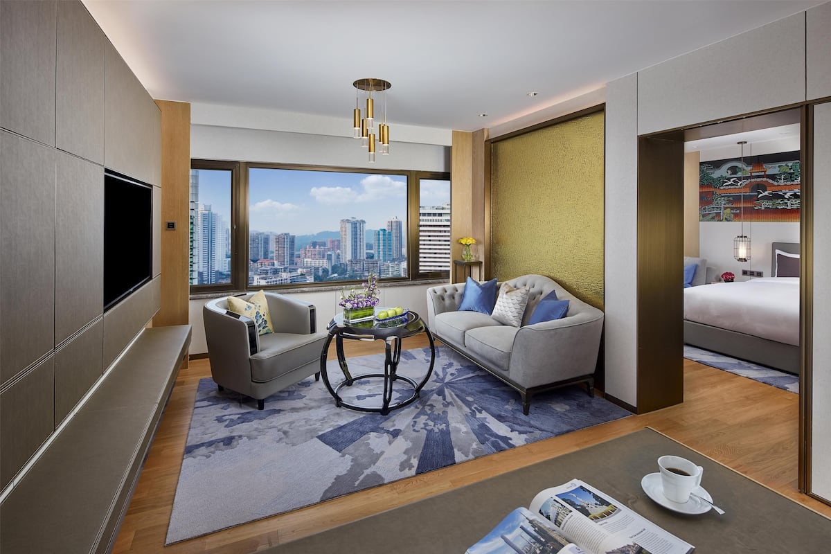 Een moderne hotelkamer met uitzicht over de stad, een bank, een stoel, een klein tafeltje met een vaas en een bed.