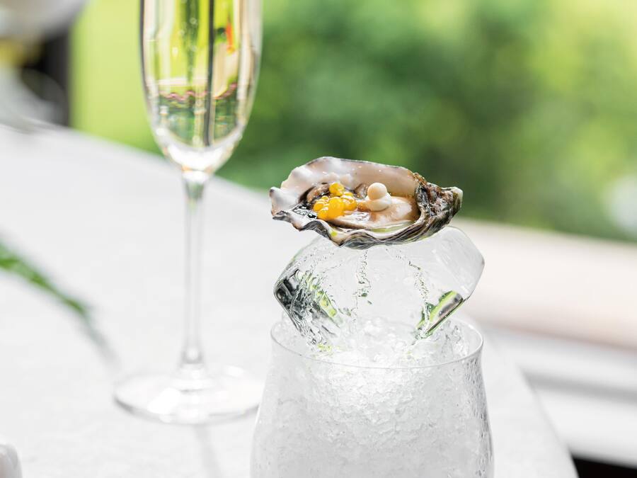 Una copa con una ostra sobre hielo, una copa de champán y un mantel blanco.