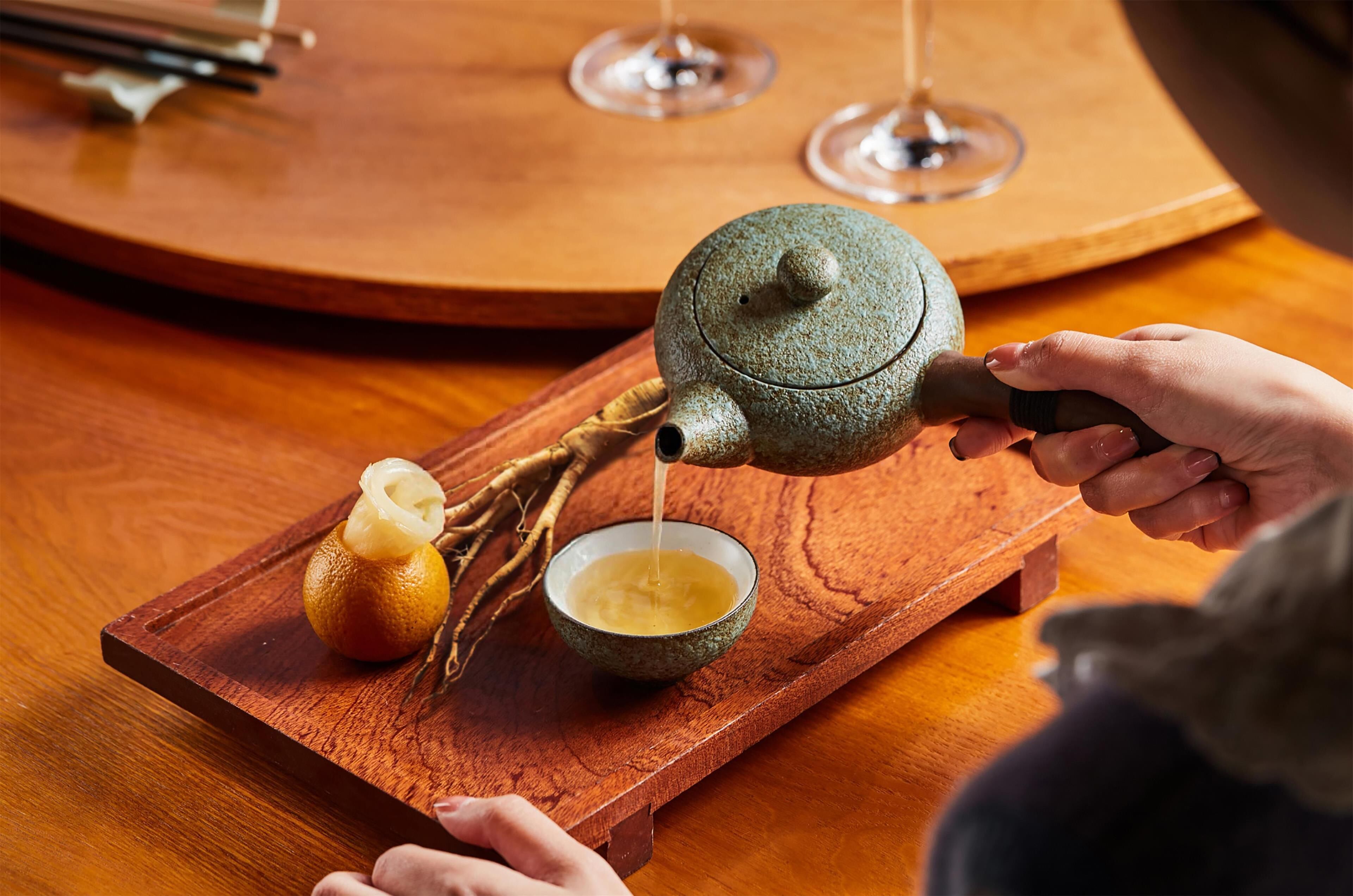 A teapot pouring tea into a cup on a wooden tray.