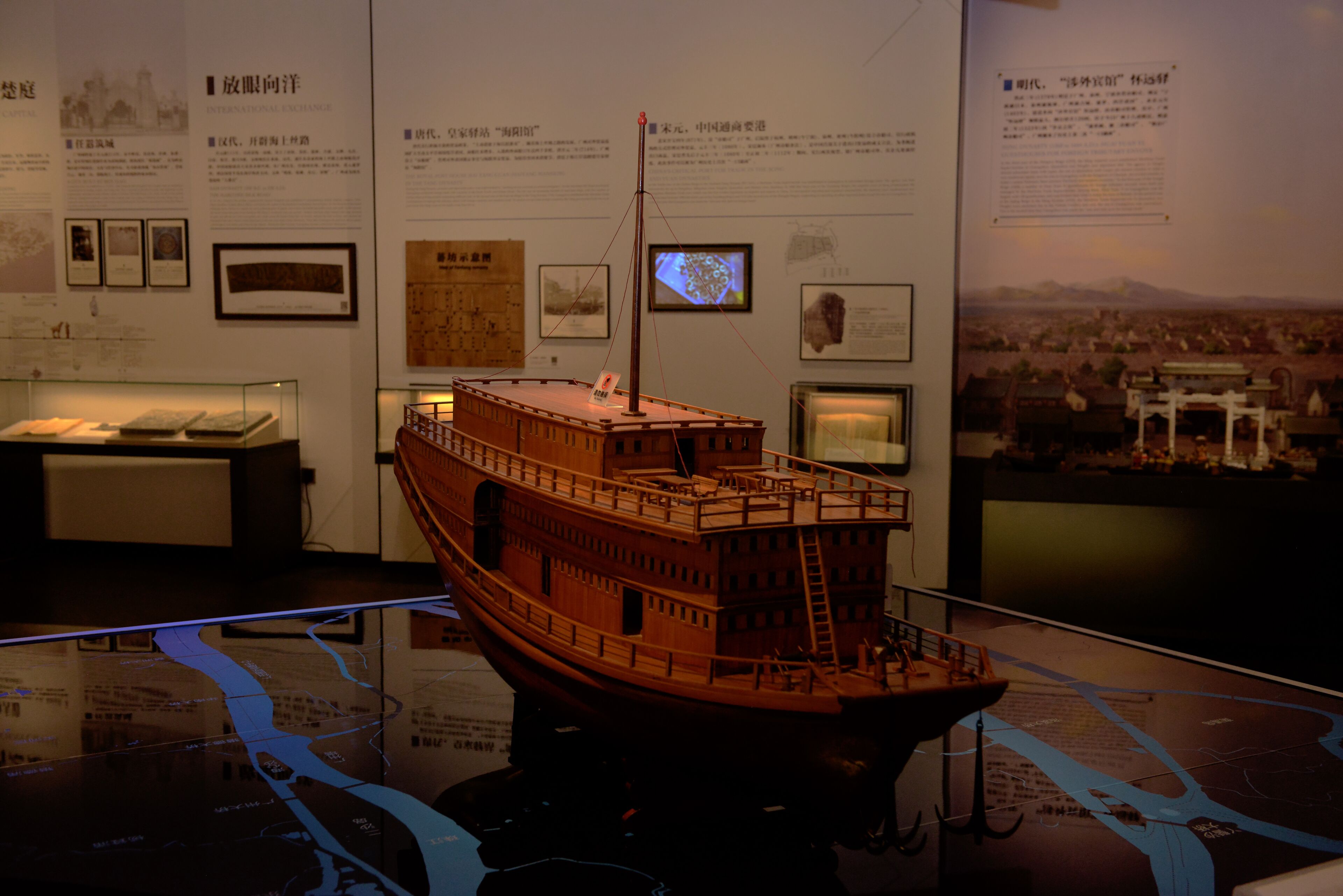 A model ship displayed in a museum setting with informational plaques and a map in the background.