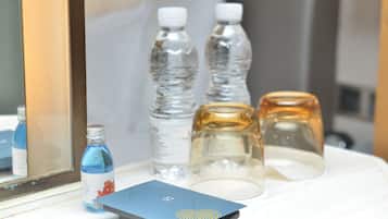 Une chambre d’hôtel avec un lit, une table de chevet et une table sur laquelle se trouvent une carte bleue, deux bouteilles d’eau et deux pots en verre.