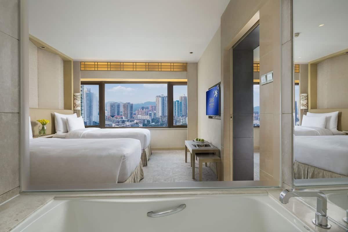 Een hotelkamer met twee bedden, een televisie, een badkuip en uitzicht over de stad.