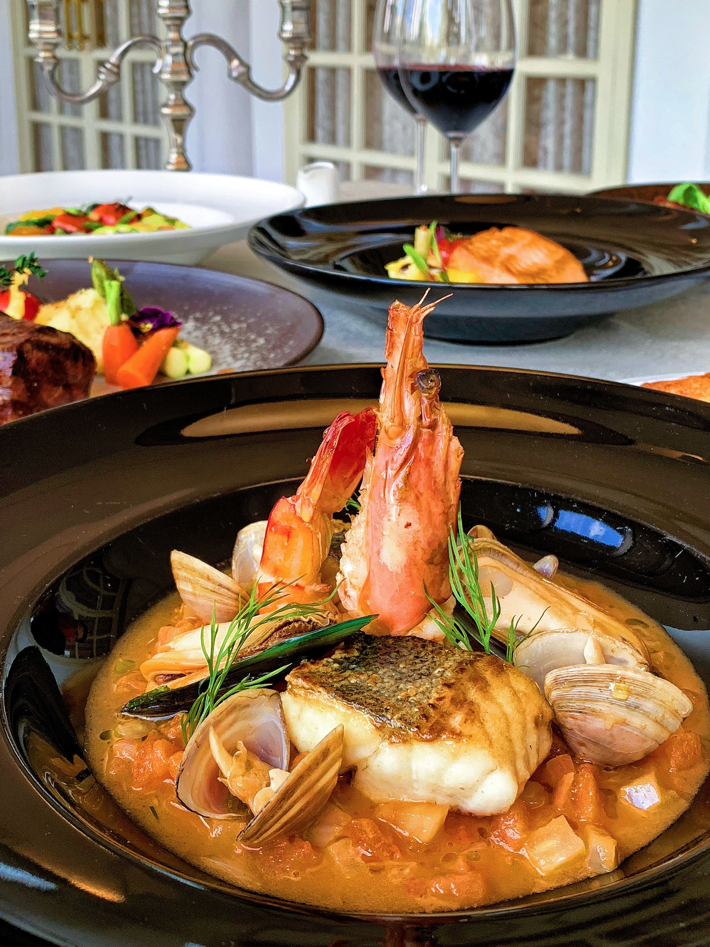 Plato de mariscos con camarones, almejas y pescado en caldo, servido sobre un plato negro.