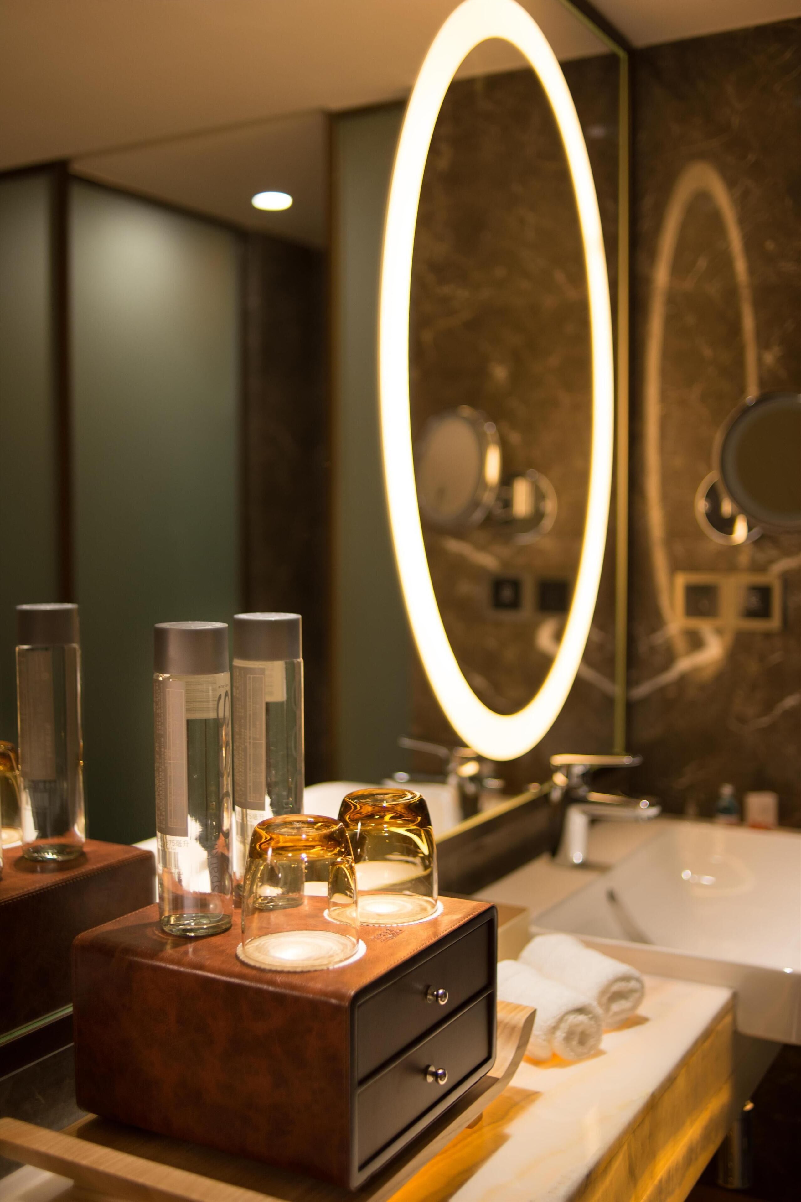 A bathroom with a vanity, a mirror with an illuminated frame, and toiletries on the counter.