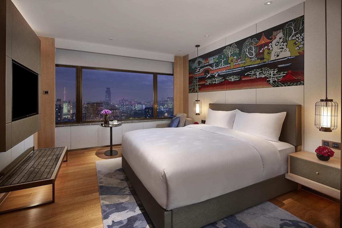 Een moderne hotelkamer met een groot bed, een bureau, een televisie en uitzicht op de stad.