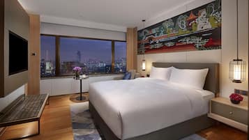 A modern hotel room with a large bed, a desk, a TV, and a city view.