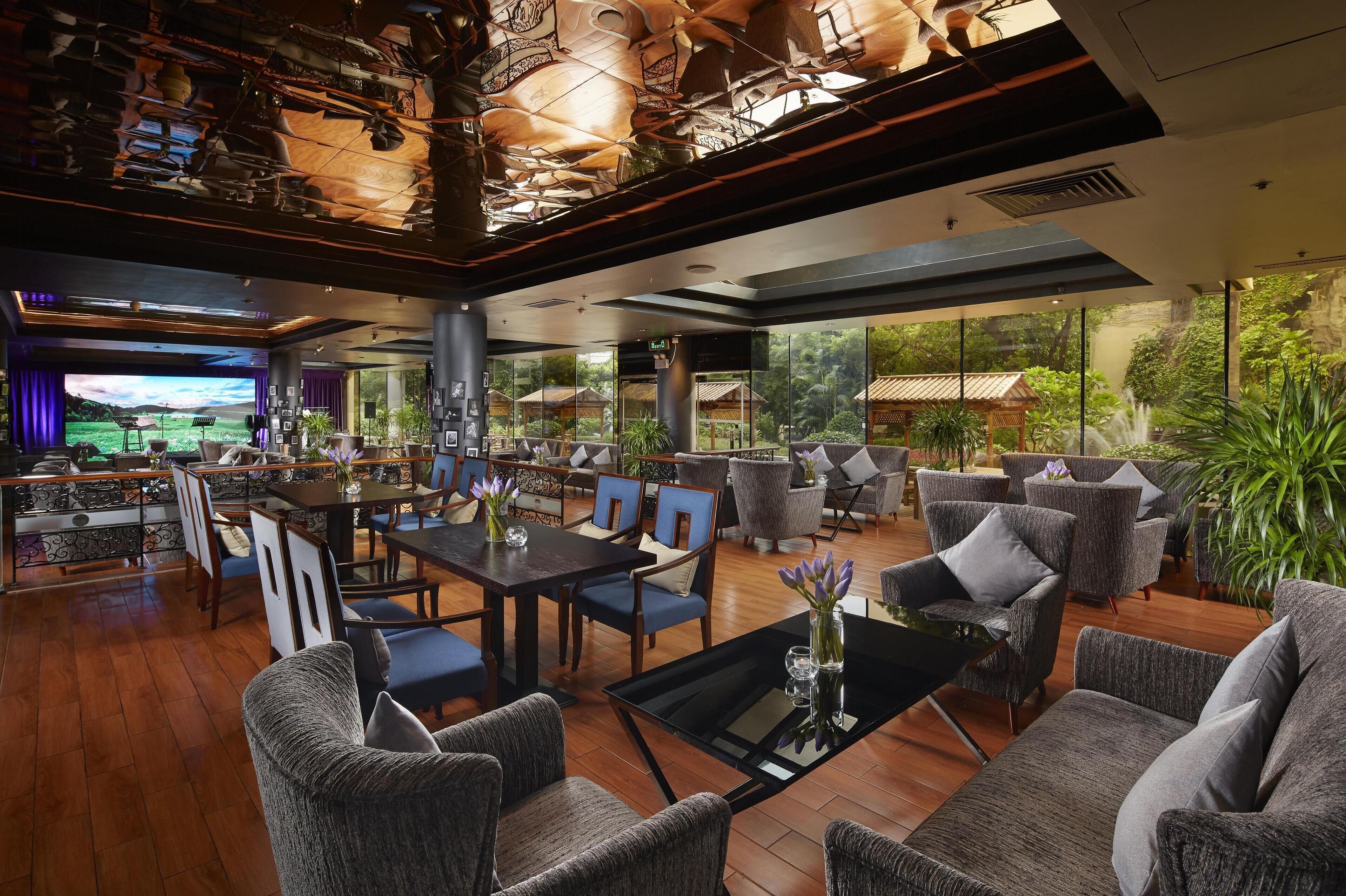 A spacious lobby with wooden flooring, modern furniture, and large windows offering a view of greenery and traditional architecture.