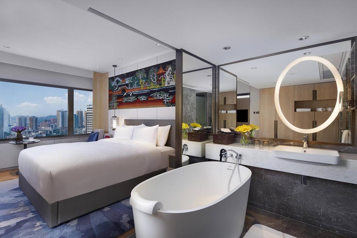 Een moderne hotelkamer met een groot bed, een badkuip, een grote spiegel en uitzicht op de stad.