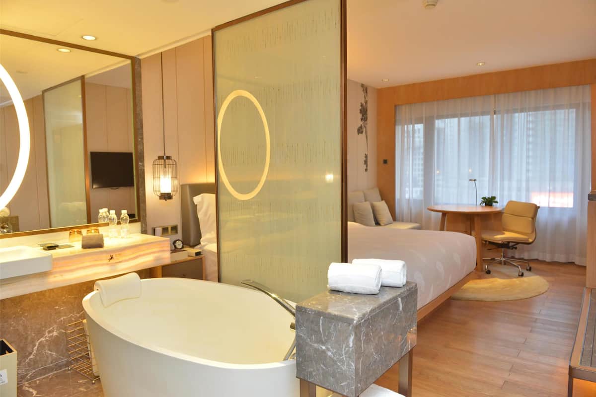 Een hotelkamer met een groot bed, een badkamer met een bad, een bureau en een stoel.