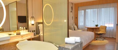 A hotel room with a large bed, a bathroom with a bathtub, a desk, and a chair.