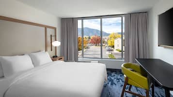 A hotel room with a large bed, a desk, and a view of autumn trees and mountains.
