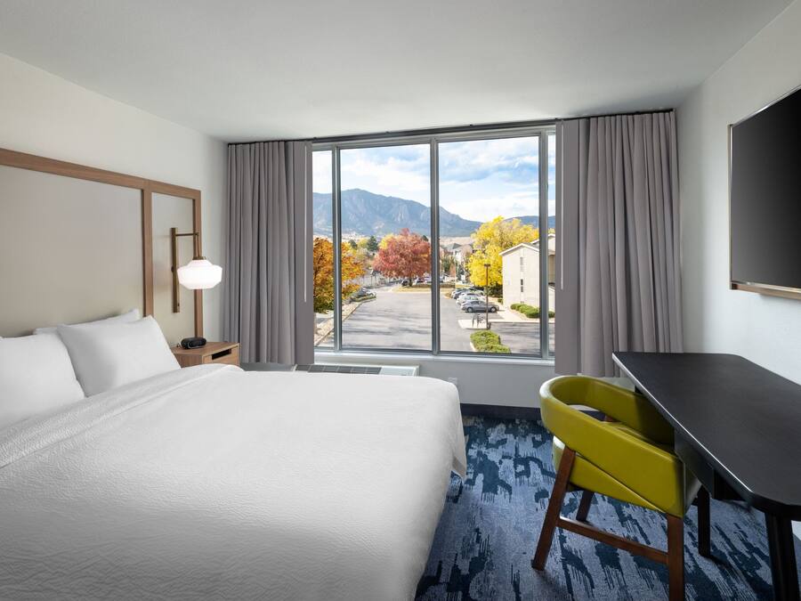 A hotel room with a large bed, a desk, and a view of autumn trees and mountains.