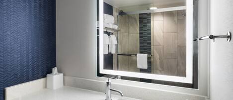 A modern bathroom with a large mirror, white sink, and a towel rack.