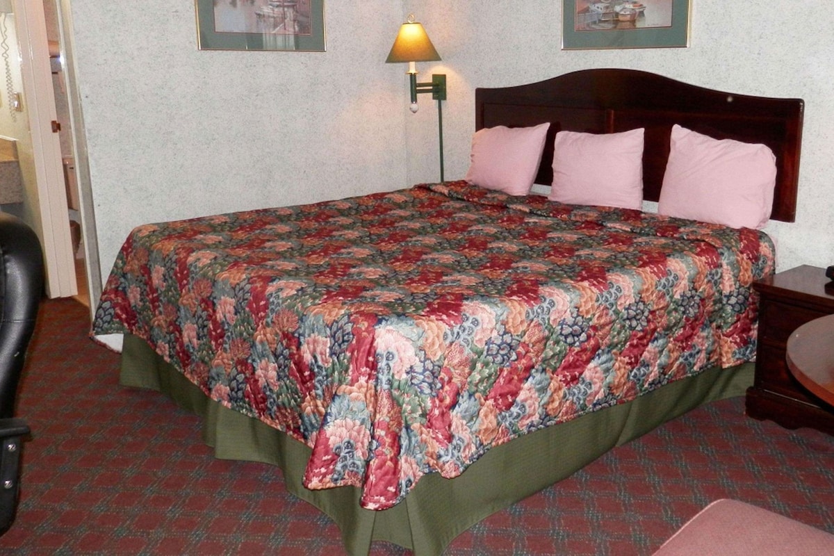 A hotel room with a bed, two bedside lamps, a chair, a small table, and a wall-mounted telephone.