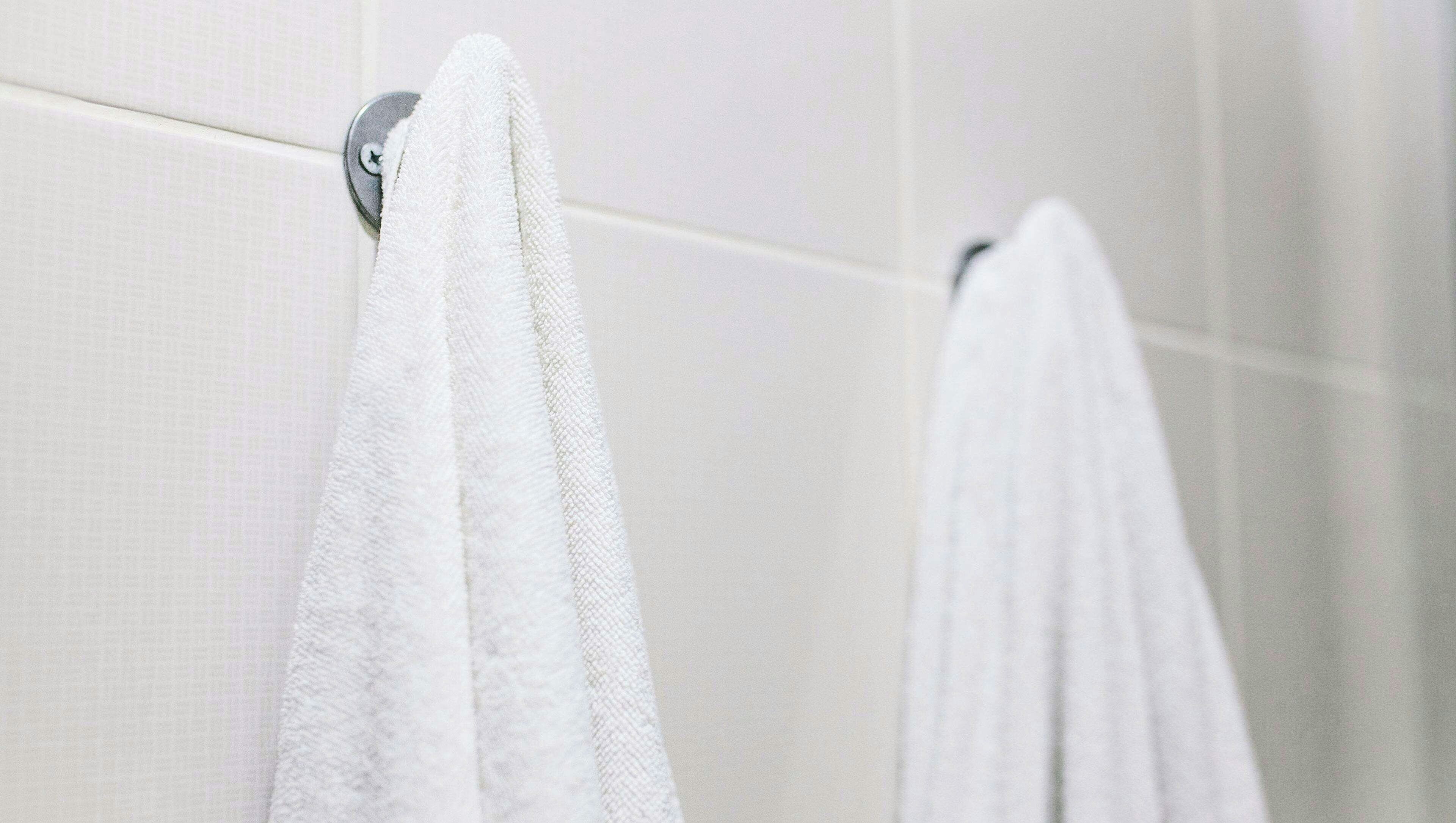 A bathroom with white tiled walls and two white towels hanging on a metal towel rack.