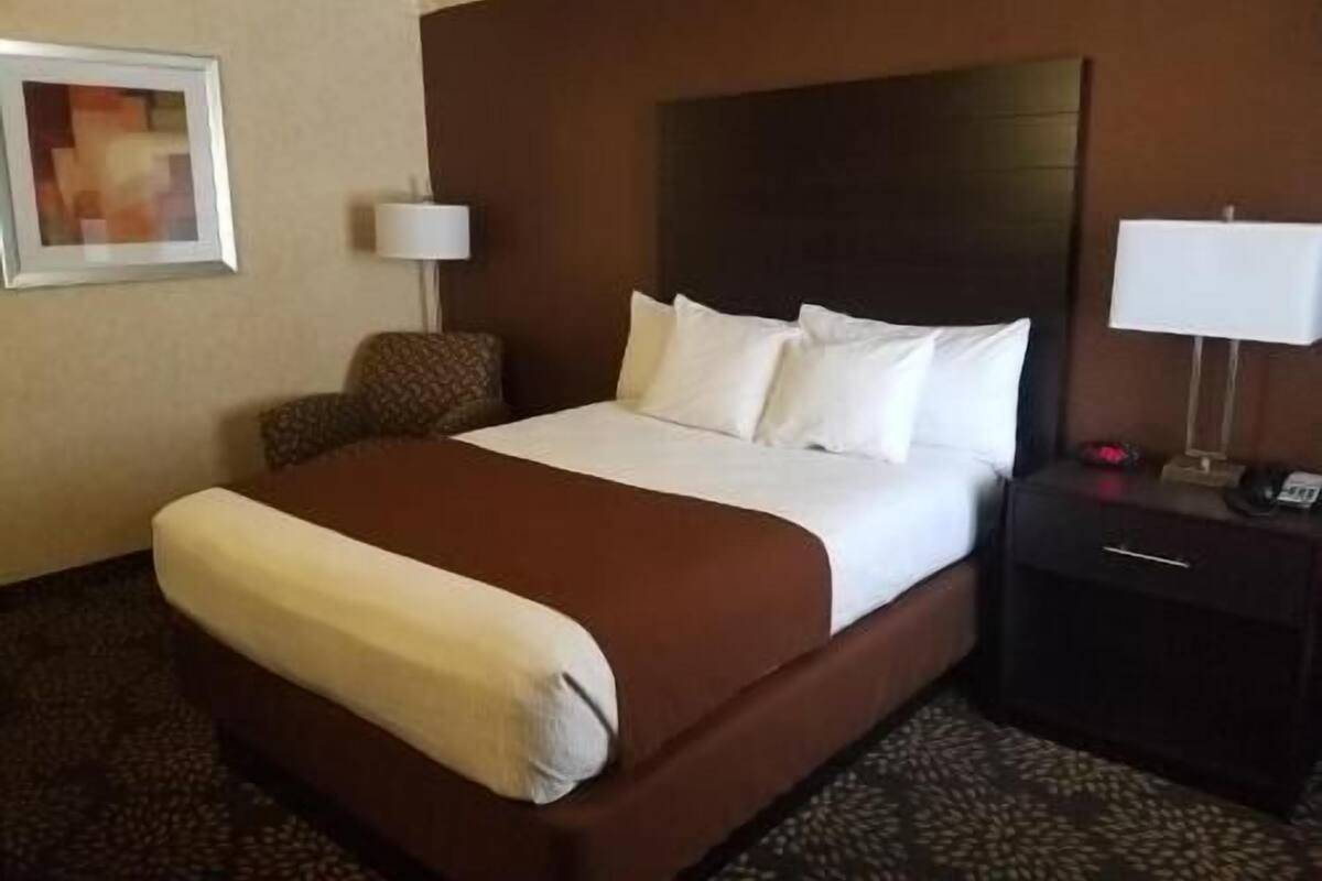 A hotel room with a large bed, a nightstand, a chair, and a framed picture on the wall.