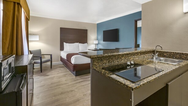 Una habitación de hotel con cama, escritorio, kitchenette y televisión.