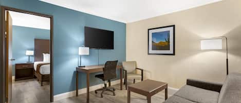 Et hotelværelse med skrivebord, stol, sofa og fjernsyn på væggen.