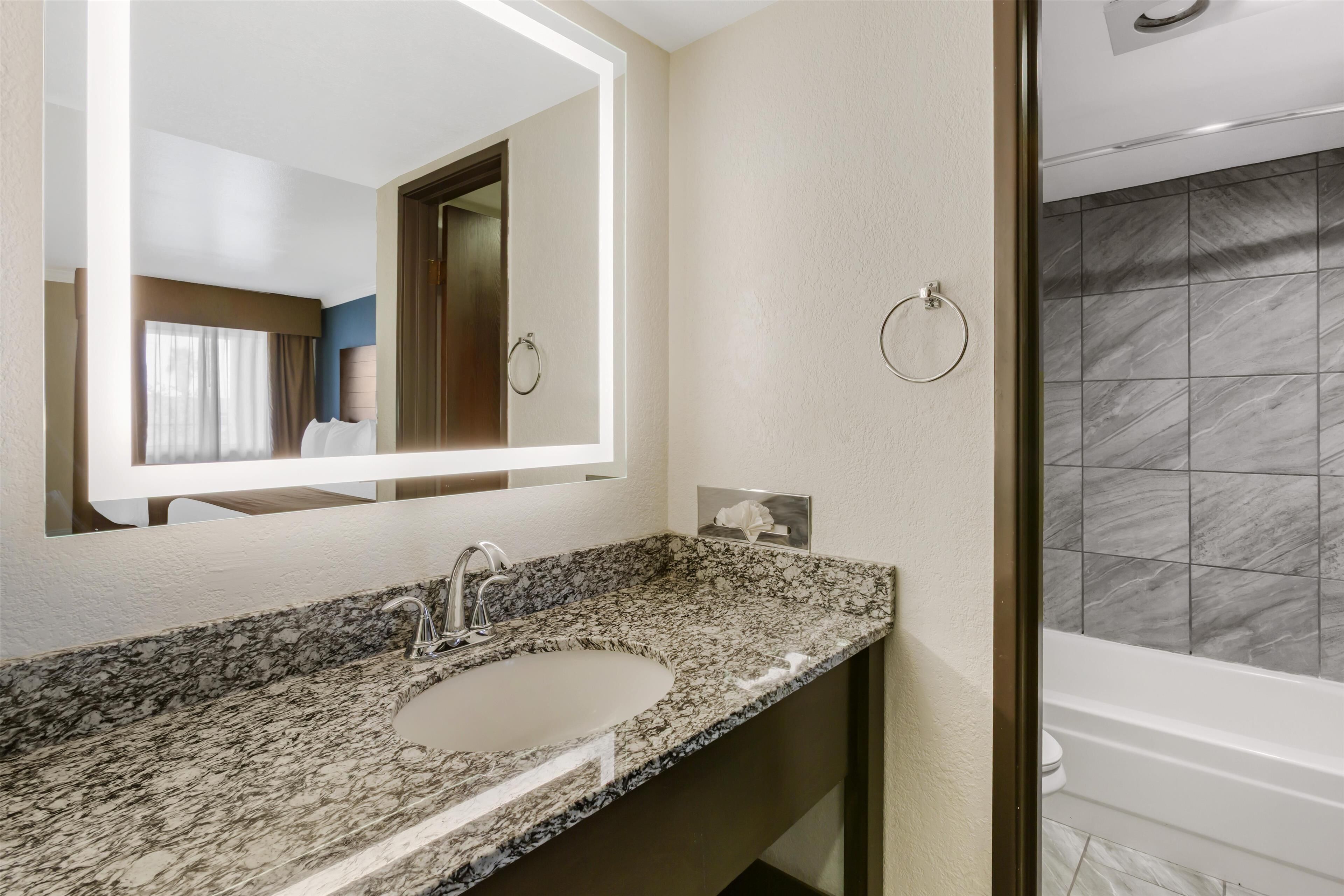 A bathroom with a granite countertop sink, a mirror, a towel ring, and a shower with dark tiles.
