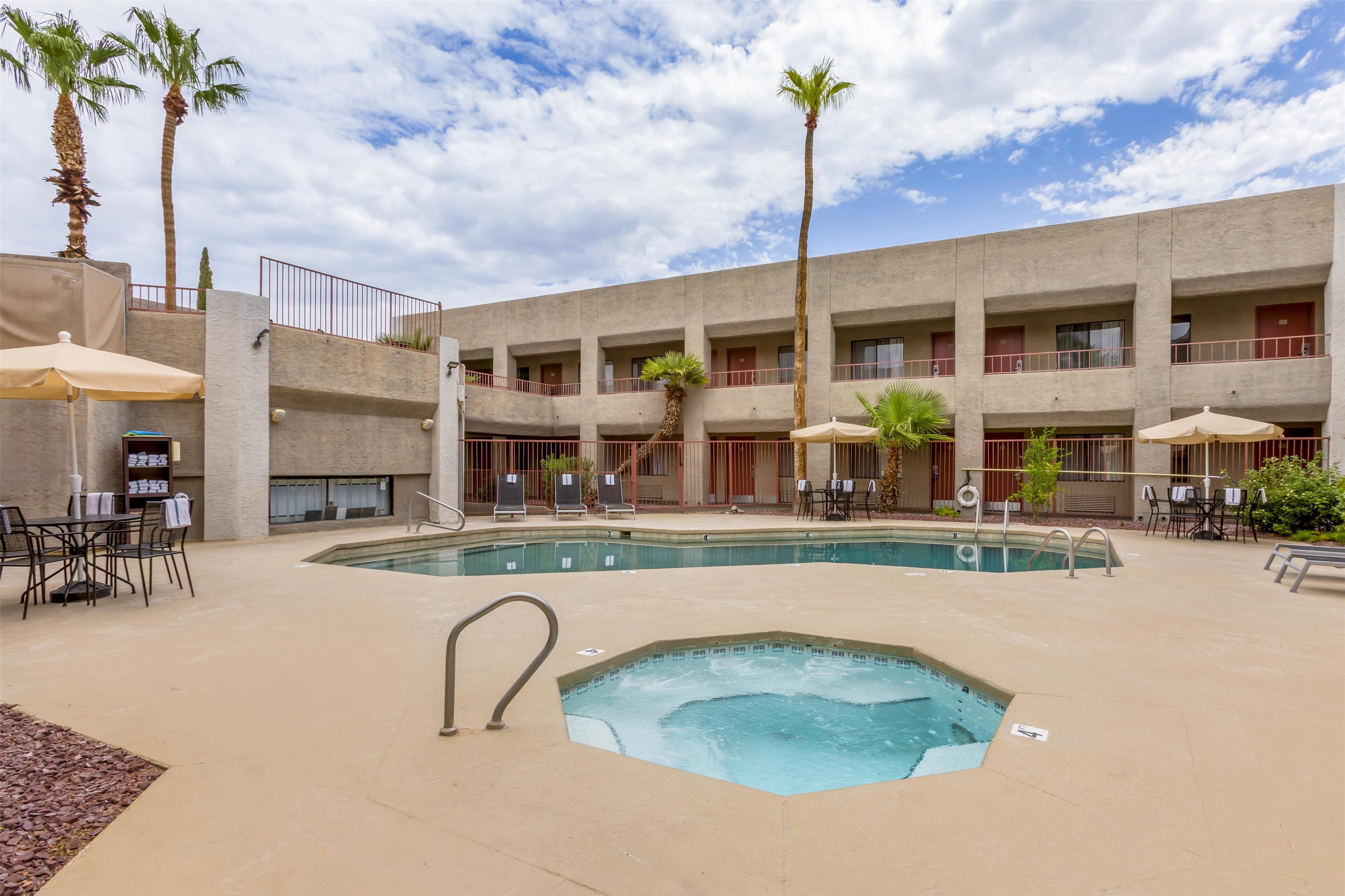 A hotel with a pool, outdoor seating, palm trees, and a multi-story building.