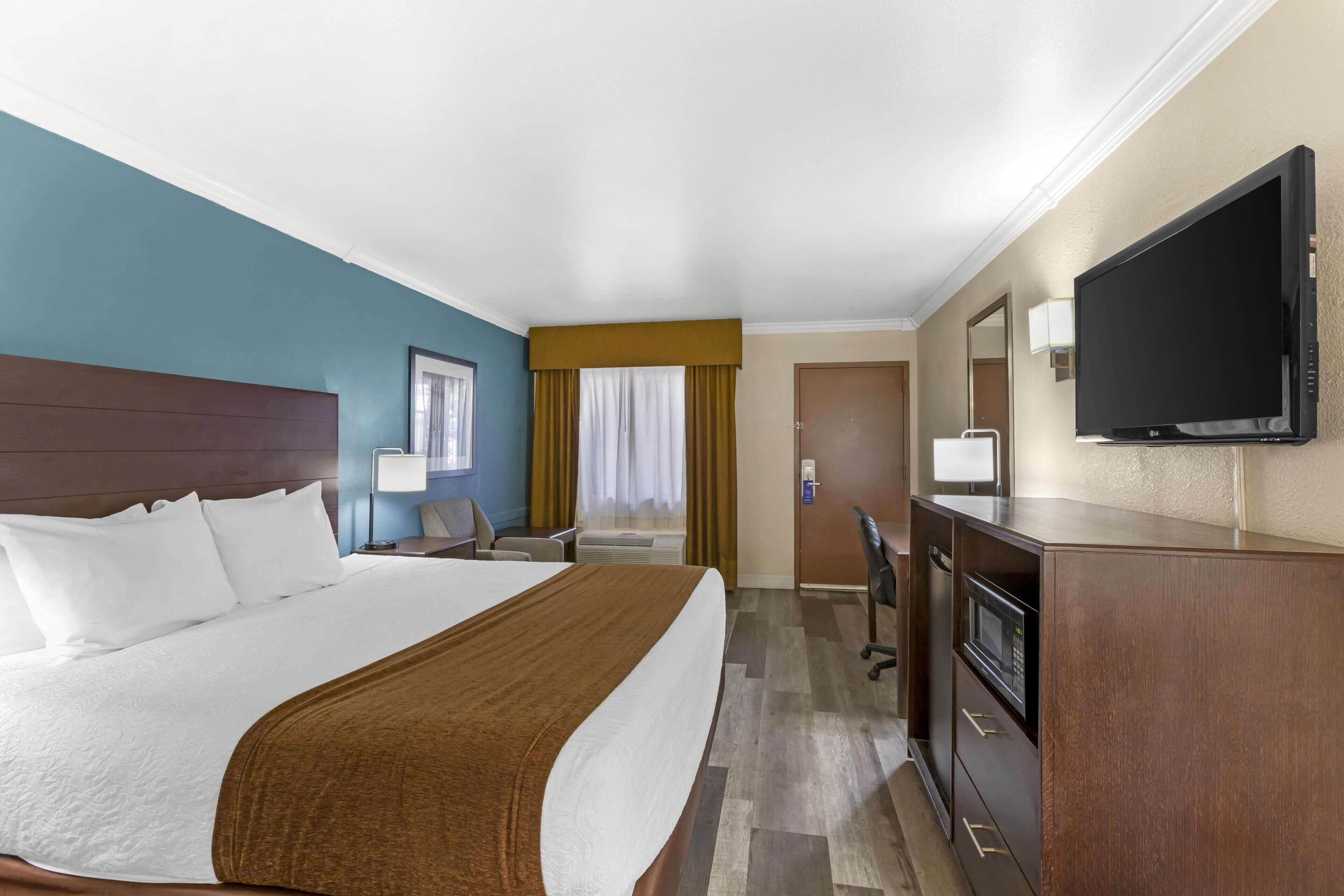 A hotel room with a large bed, a desk with a computer, a TV, and a microwave.