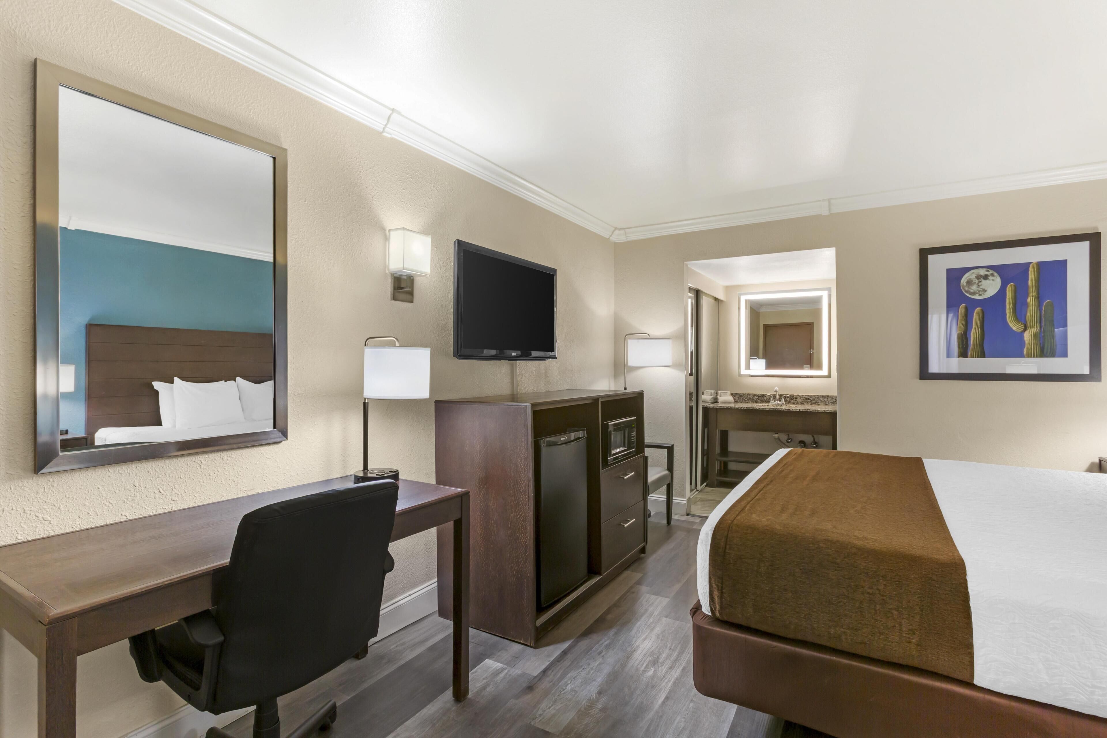A hotel room with a bed, desk, chair, television, and artwork.