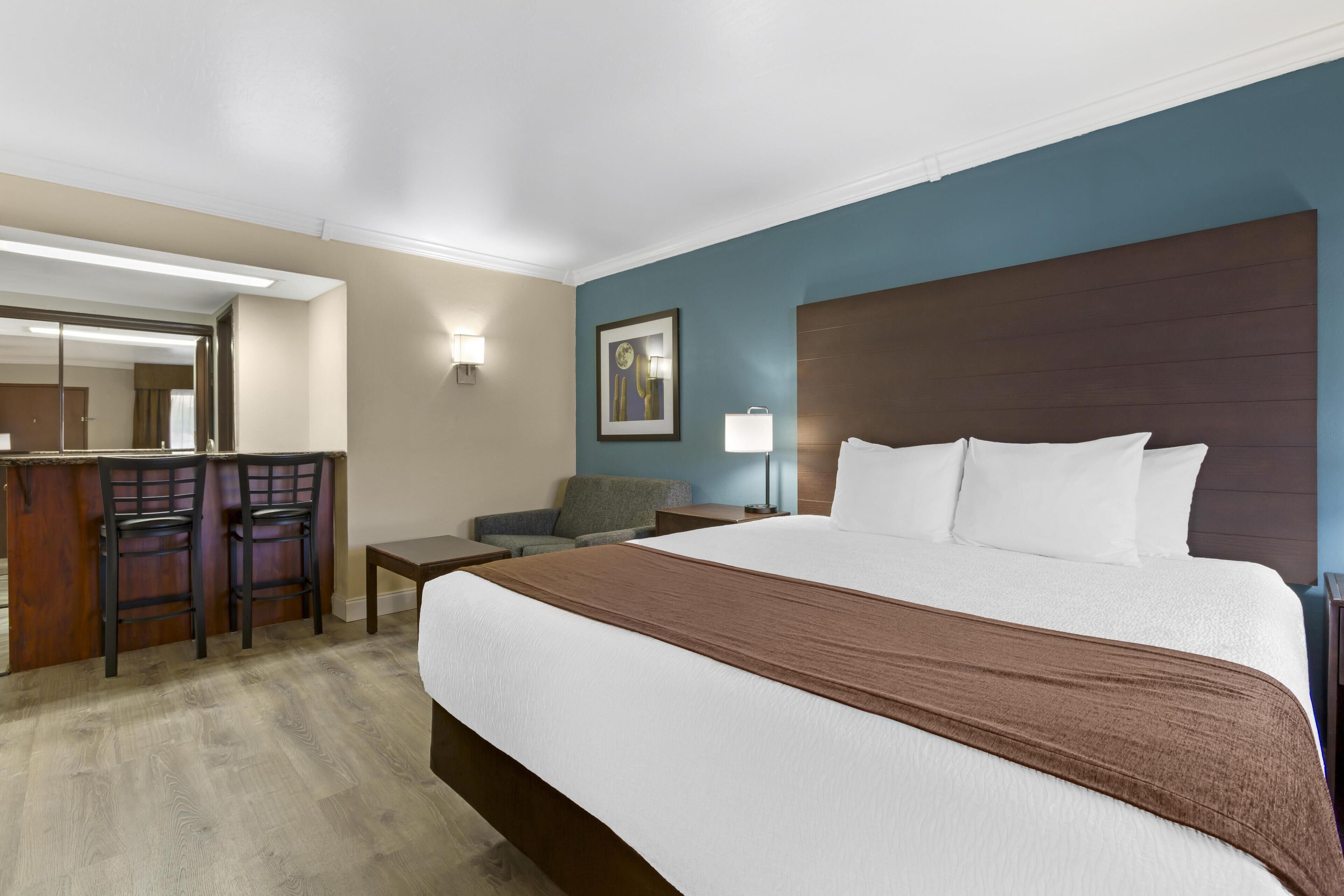 A hotel room with a large bed, a desk with a chair, a small table, and a sofa.