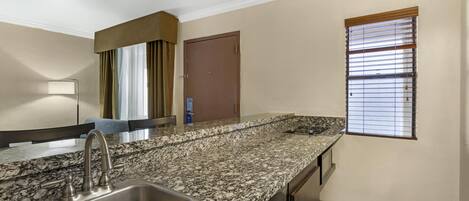 A kitchen with a granite countertop, stainless steel sink, and a window with blinds.