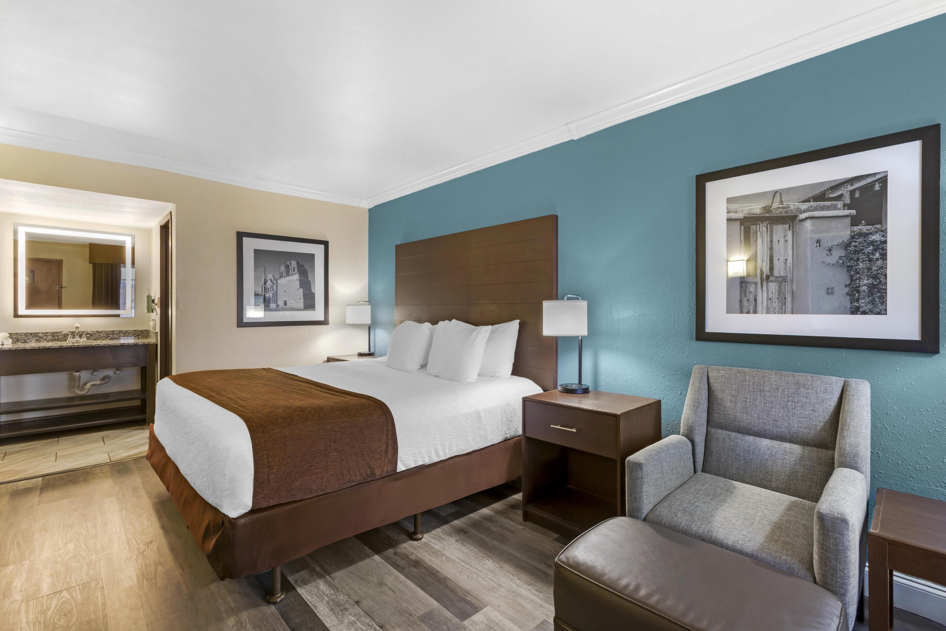 A hotel room with a bed, bedside table, chair, and a large framed picture on the wall.