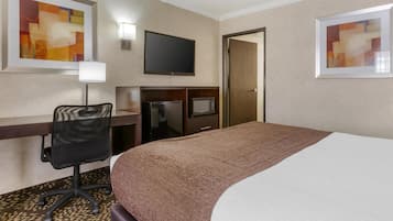 A hotel room with a bed, desk, chair, television, and artwork on the walls.