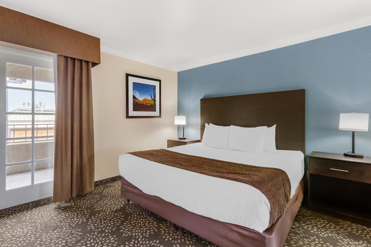 A hotel room with a large bed, a nightstand, a lamp, a picture on the wall, and a window with curtains.