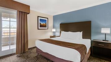 A hotel room with a large bed, a nightstand, a lamp, a picture on the wall, and a window with curtains.
