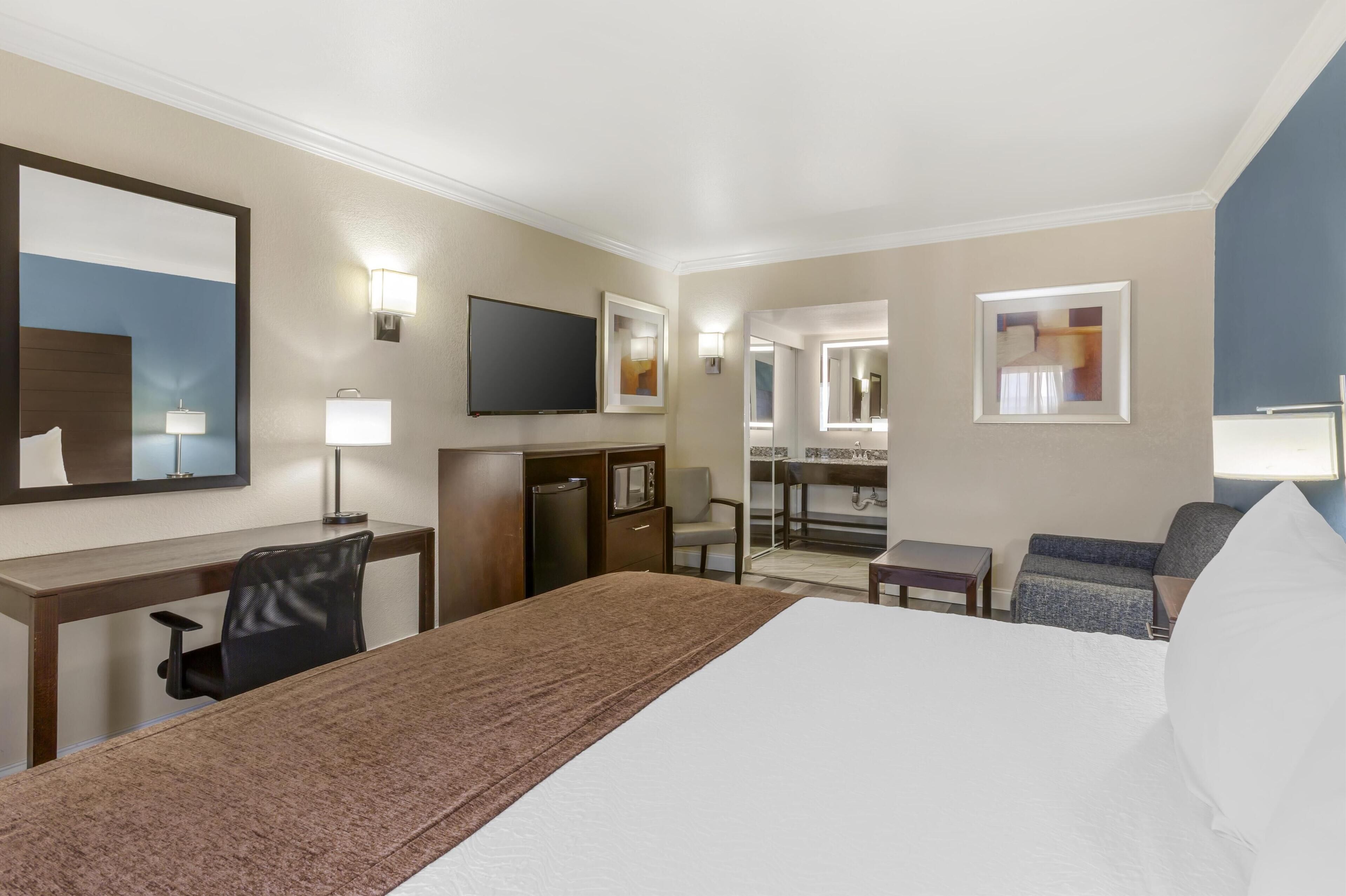 Hotelkamer met een groot bed, een bureau met stoel, een televisie, een magnetron, een klein tafeltje en een bank.